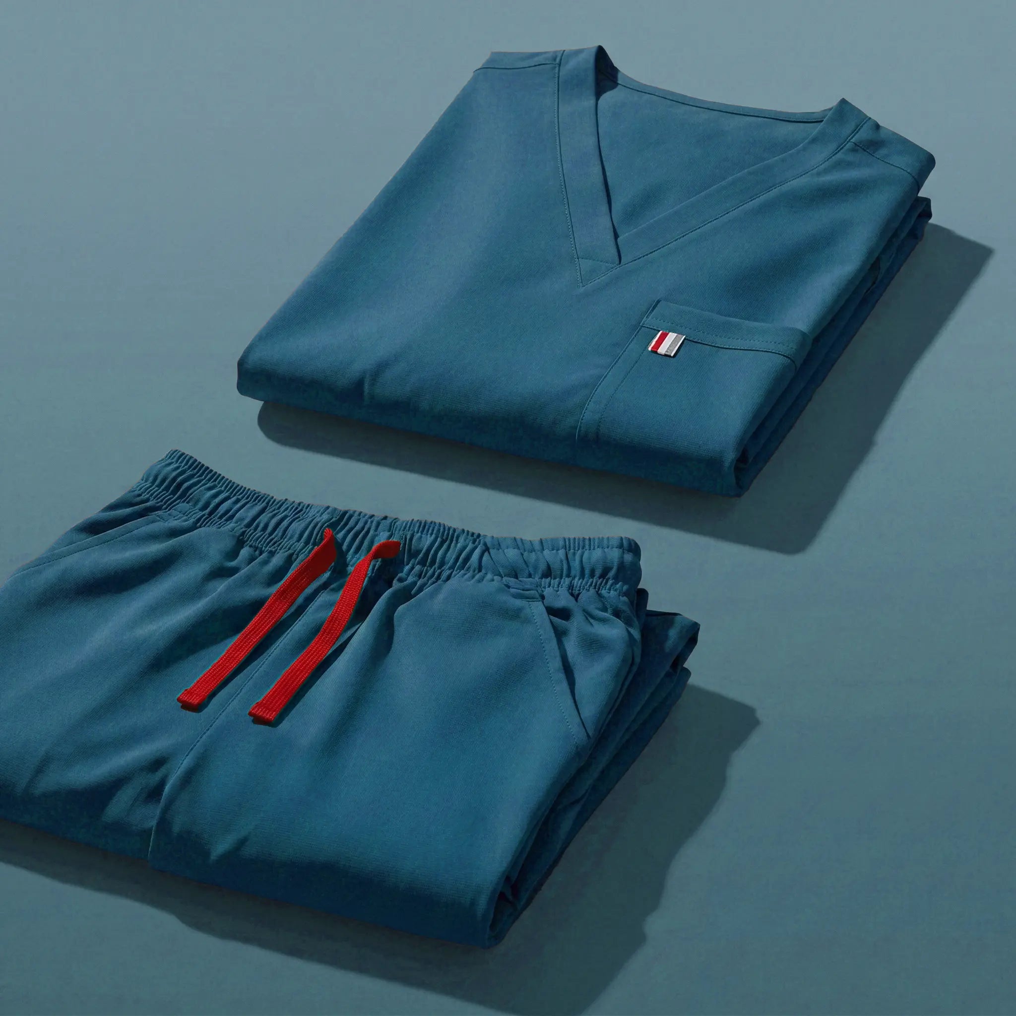 aerial view of caribbean blue mediclo scrub tops and pants folded neatly on a studio floor.