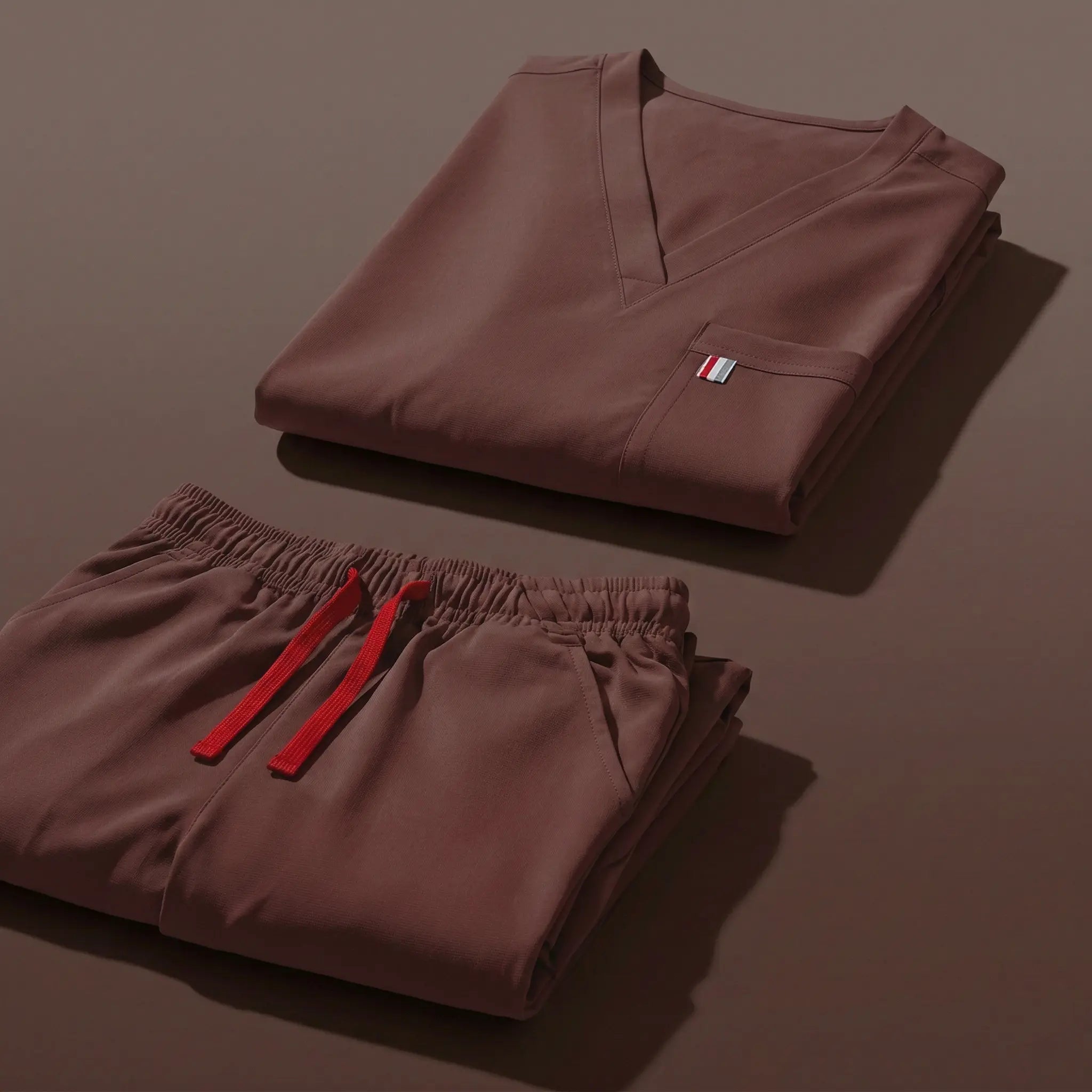 aerial view of coffee brown mediclo scrub tops and pants folded neatly on a studio floor.