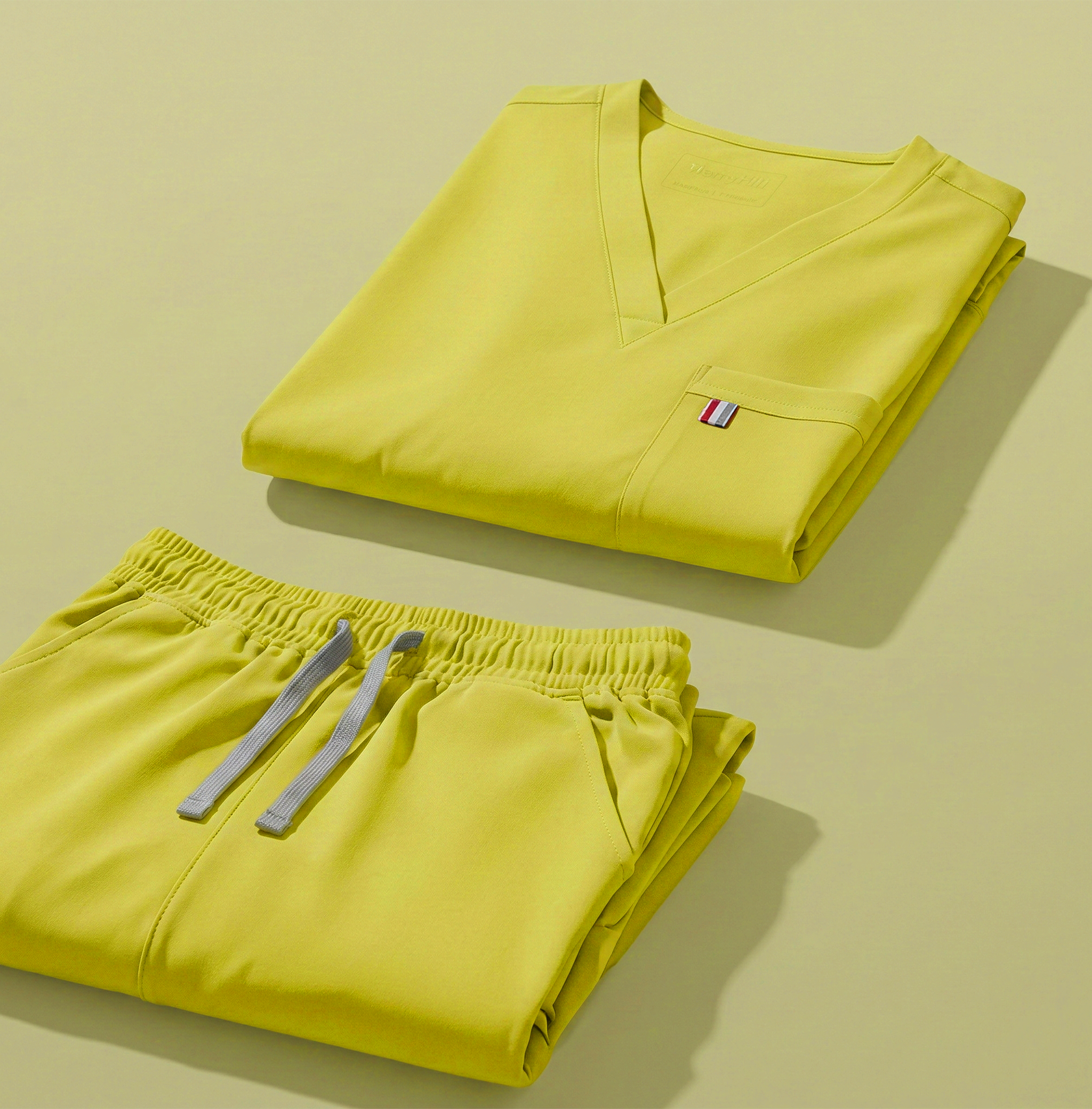aerial view of lemon yellow mediclo scrub tops and pants folded neatly on a studio floor.
