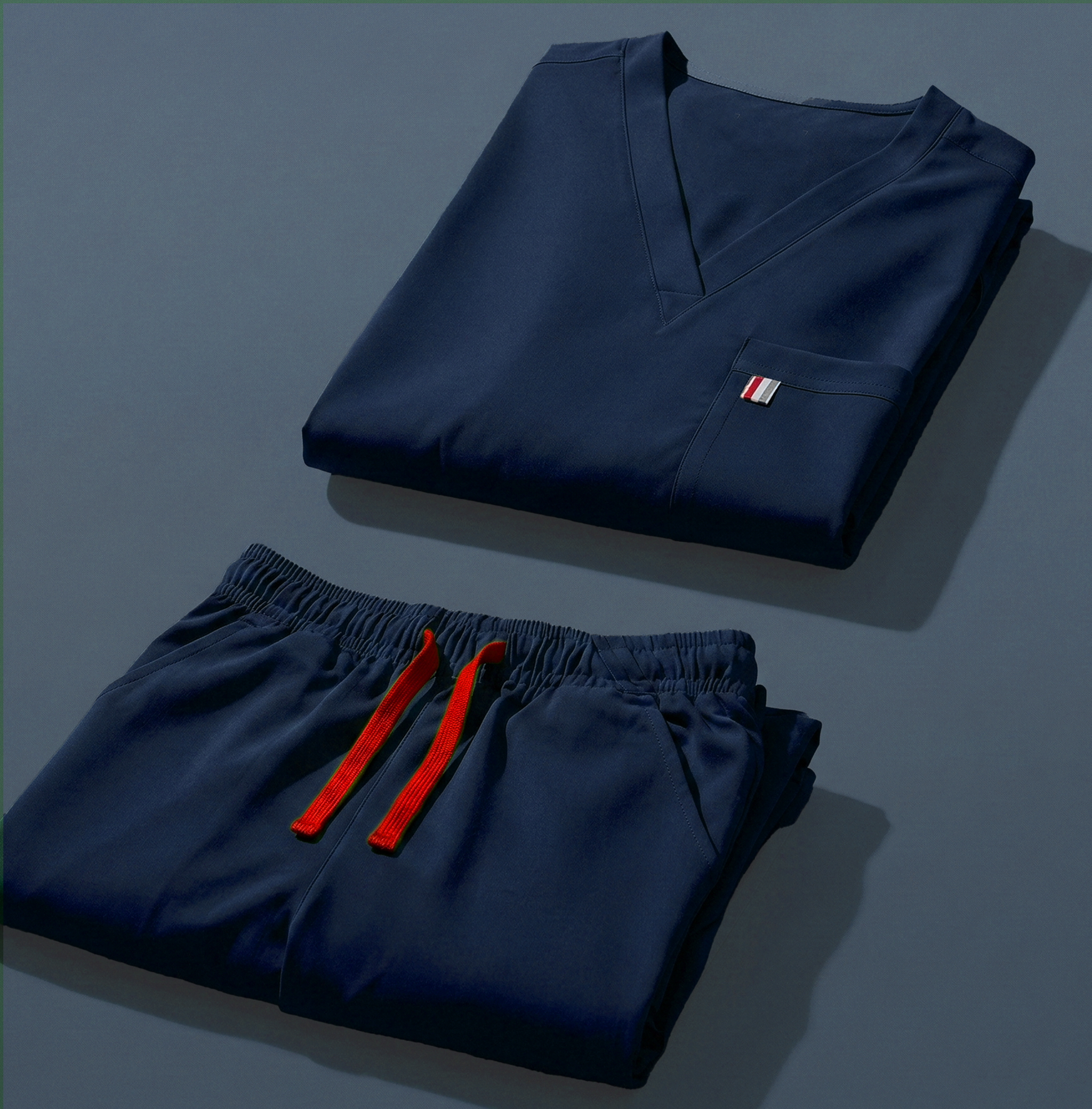 aerial view of navy mediclo scrub tops and pants folded neatly on a studio floor.