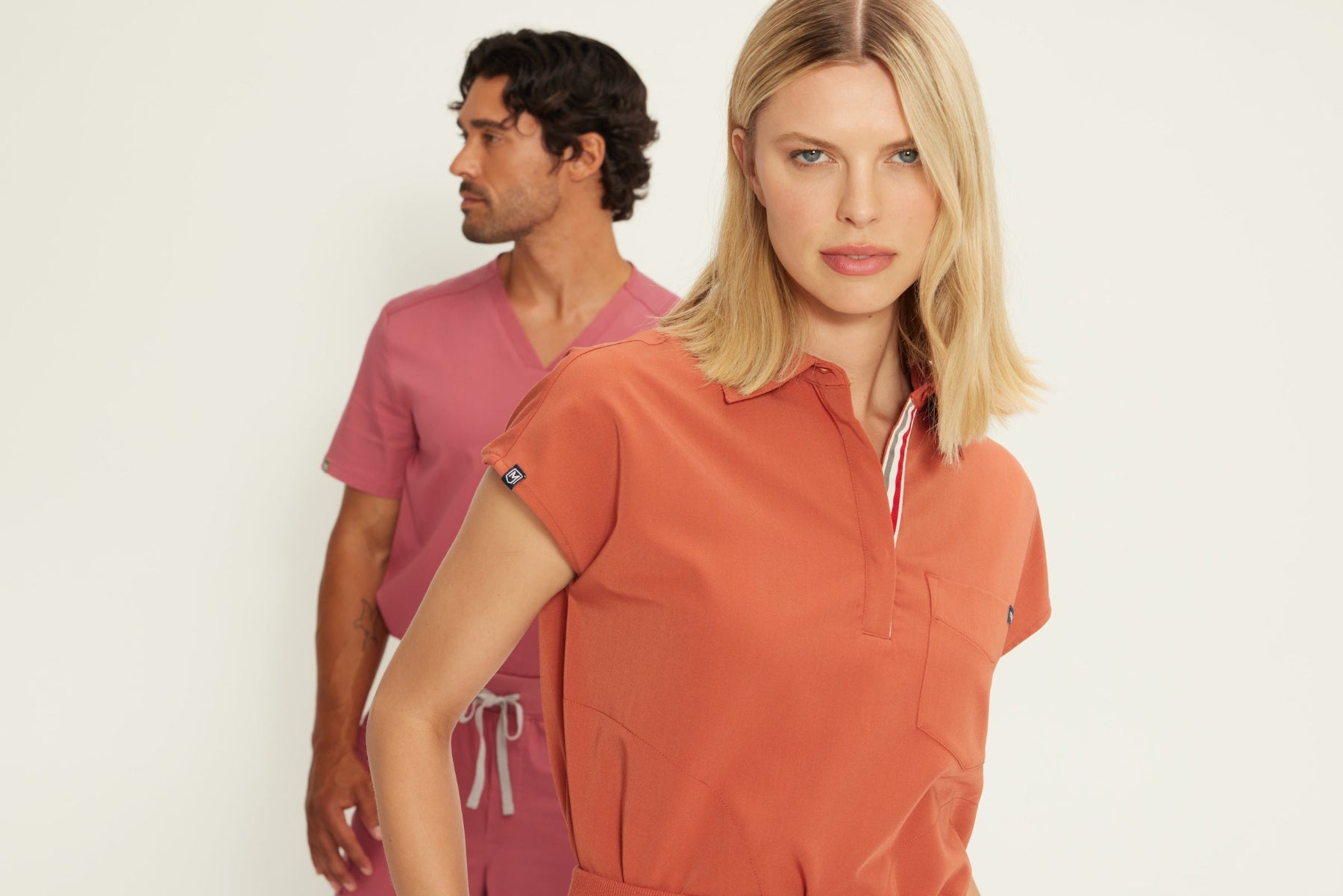 a male and female nurse wearing fysel scrub sets in terracotta and mauve.
